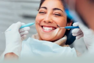 A smiling woman receives a dental exam from a professional wearing white gloves and using dental tools.