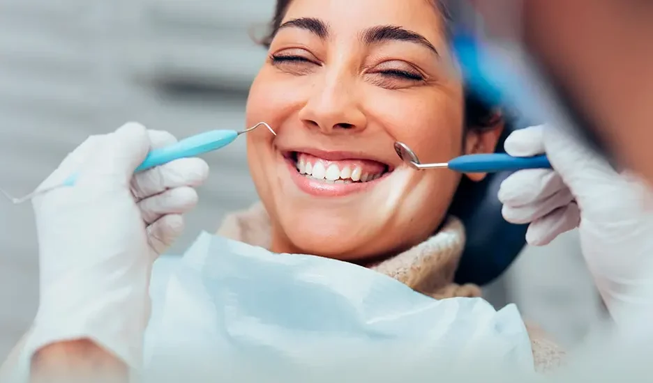 A smiling woman receives a dental exam from a professional wearing white gloves and using dental tools.