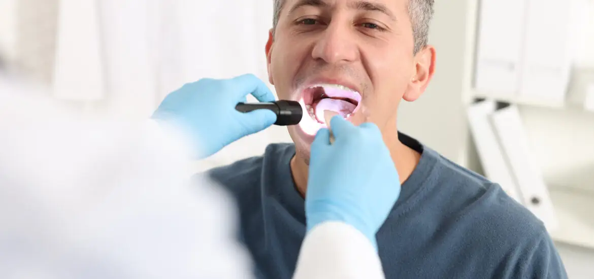 A doctor examines a man's mouth with a flashlight device in a clinic.