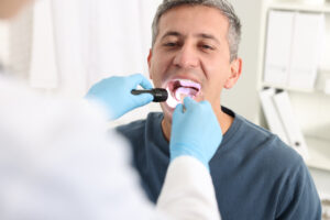 A doctor examines a man's mouth with a flashlight device in a clinic.