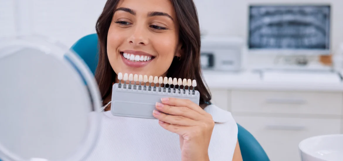 Patient comparing tooth shades during a professional teeth whitening consultation at a dental office.