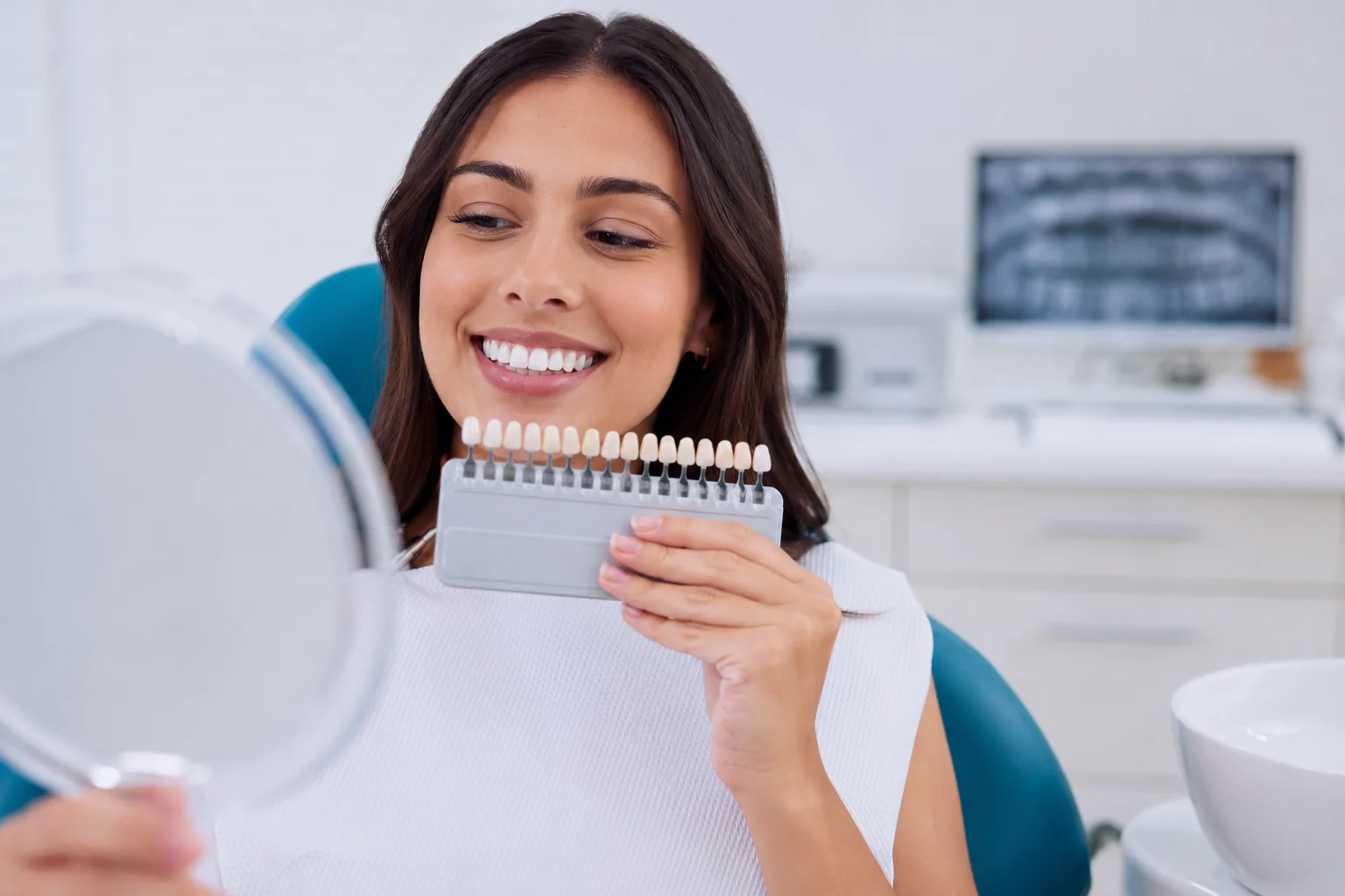 Patient comparing tooth shades during a professional teeth whitening consultation at a dental office.